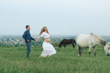 Rural couple on a green meadow communicates with animals. Pregnant wife. Therapy and relaxation for pregnant women