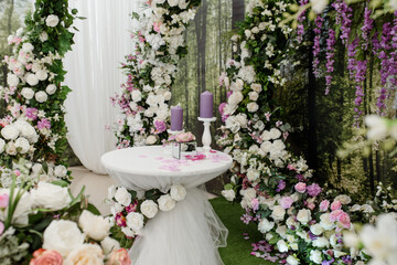 Wedding ceremony arch decorated with roses. In the middle is a table with candle composition.