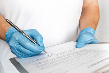Close-up of professional medical man therapist hands in blue gloves signing medical document on clipboard. Concept of healthcare, medicine and insurance.filling out medical documentation