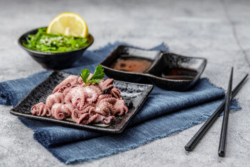 Traditional japanese or seafood concept. Delicious and healthy boiled mini octopus and wakame or seaweed salad with soy sauce and lemon served with chopstick.