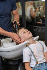 Obraz na płótnie Canvas a blonde boy gets his hair washed in a barber shop before cutting his hair.