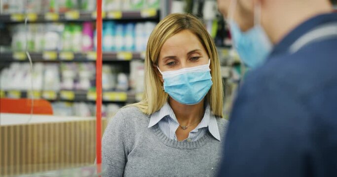 Authentic Shot Of Female Customer And Male Cashier Wearing Medical Masks To Protect Themselves From Disease While Paying With Credit Card Grocery Food Products In Supermarket.