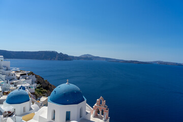 Fototapeta na wymiar Iconic view of Santorini, with typical blue dome church, sea and white facades. Detail of the roof of an orthodox church. Blue domed church along caldera edge in Oia, Santorini