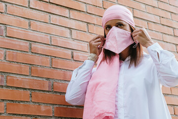 Woman putting on a pink mask and wearing a pink scarf from the breast cancer. Lifestyle. health