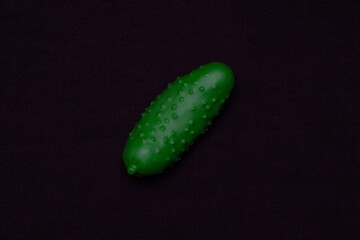 Green cucumber on a dark background. Plastic toy