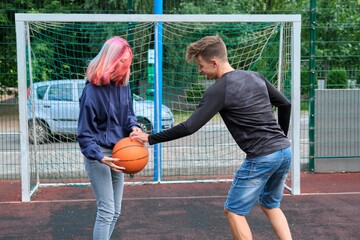 Teenagers boy and girl playing street basketball together