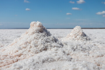 White pink salt bunches collecting. Close-up shining sea salt on coast of salt lake with blue sky...