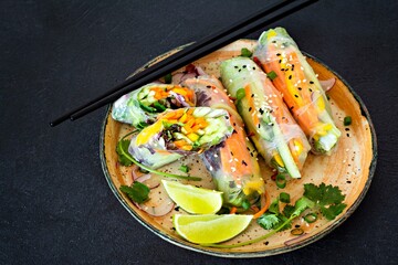 Fresh Asian appetizer Spring rolls (Nem) made from rice paper and raw vegetables and herbs with hot sauce on a dark background. Vietnamese Food
