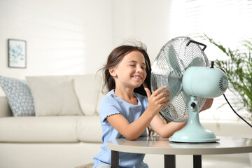 Little girl enjoying air flow from fan at home. Summer heat - obrazy, fototapety, plakaty