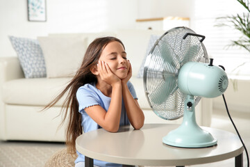 Fototapeta Little girl enjoying air flow from fan at home. Summer heat obraz