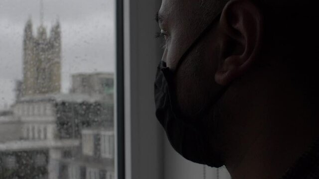 Adult Male Wearing Face Mask Looking Out Rainy Window. Locked Off