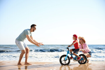 Happy parents teaching son to ride bicycle on sandy beach near sea