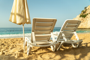 Empty Beach chairs and a yellow sun umbrella await tourists against the backdrop of the blue sea and beautiful ocean waves and blue sky. Beautiful seashore beach resort.