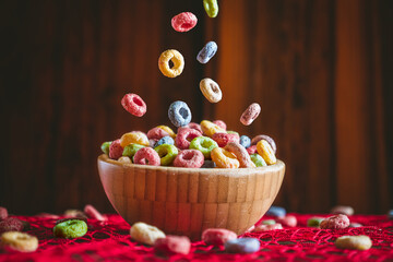 Colorful round fruit cereals falling into a wooden bowl on a red table. Preparing breakfast. 