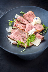 Modern Style traditioneller Beefsteak Aufschnitt mit Rucola Salat und Parmesan Käse angeboten als Draufsicht auf einem Modern Design Teller
