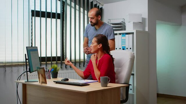 Hispanic woman asking collague for help sitting in front of pc in modern office. Team working in professional workplace in personal corporate company typing on computer keyboard looking at desktop