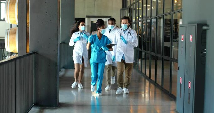 Mixed-races team of males and female doctors and nurses running and rushing at corridor of hospital. Multi ethnic medics in medical masks run in clinic. Emergency call. Saving lives.