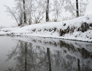 Reflection of snow covered snow back along city park river of Alberta