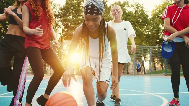 Four multi-ethnic girls dancing training out while their team leader bouncing basketball ball. Beautiful female basketball team. Mixed-race youth. Hobby and activities.