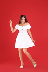 Young woman wearing stylish white dress on red background