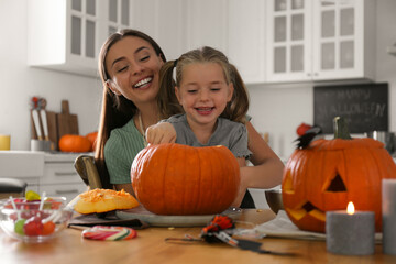 Mother and daughter making pumpkin jack o'lantern at table in kitchen. Halloween celebration