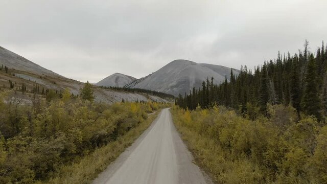 View of Scenic Road from Above surrounded by Mountains and Forest on a Cloudy Fall Day. Aerial Drone Shot. Taken near the Dempster Highway, Yukon, Canada.