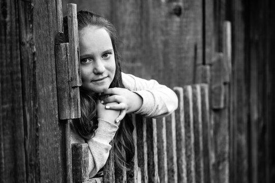 Portrait of teengirl standing near vintage rural fence. Black-and-white photography.