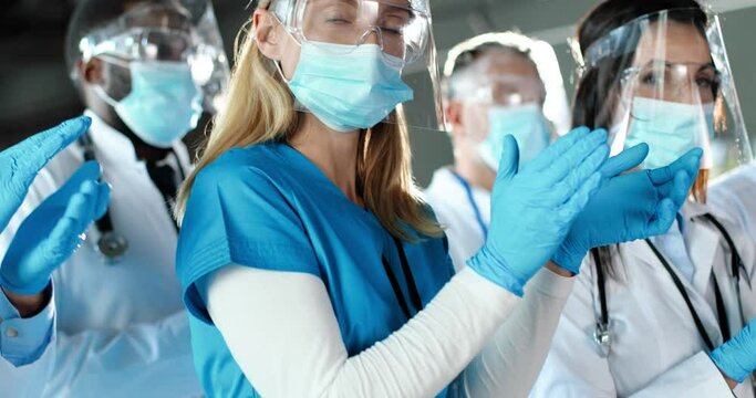 Close up of mixed-races professionals males and females doctors applauding in hospital. International group of medics in masks. Applause. Multi ethnic physicians in protection in clinic. Covid-19.