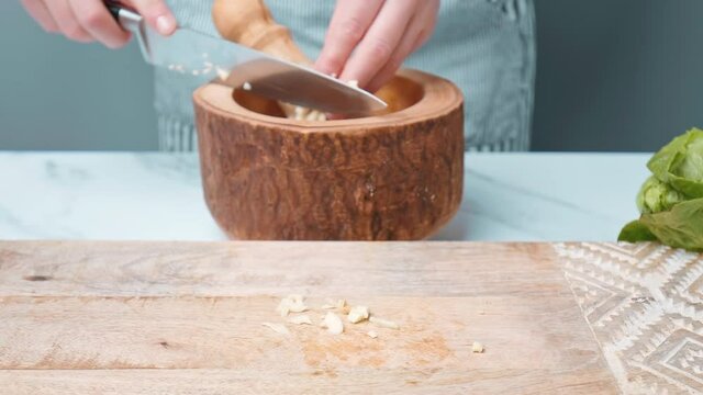 Chopping garlic on a wooden board for Caesar Salad dressing sauce in 4k. Close up of womans hands, finely cutting garlic and crashing it for a salad sauce.