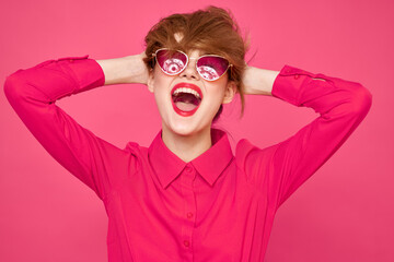 Cheerful woman in sunglasses touching hair with hands and pink shirt cropped view