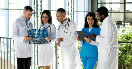 Multi ethnic doctors, men and women, standing in clinic, talking and discussing diagnosis....