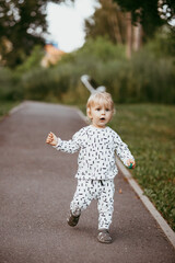 boy walking in a beautiful white suit against the background of nature, baby about one year old learning and playing outdoors.