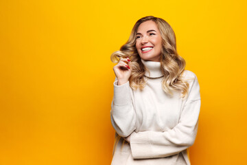 Smiling confident blonde woman with curly hair dressed in white sweater, stand with hands crossed,...