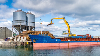 Crane with wood logs gripple loading timber on cargo ship for export in Wicklow commercial port. Transport industry in Ireland