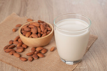 Almond milk in glass with almond seed in wooden bowl   on table.