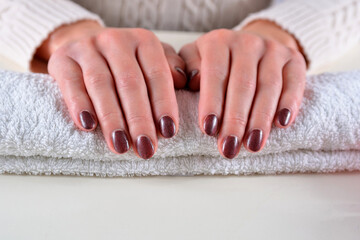 Girl hands with brown nails polish color on a towel in a beauty salon on a white desk. Manicure and beauty concept