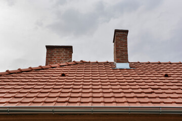Home roof with red tiles and dramatic rains clouds in the background. Weather disasters concept