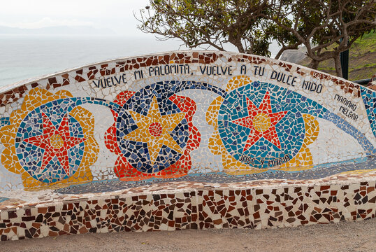 Miraflores, Peru - December 4, 2008: Parque del Amor, Love Park. Artful bench decorated with colorful faience pieces with green foliage over and part of ocean visible. Mariano Melgar poem.