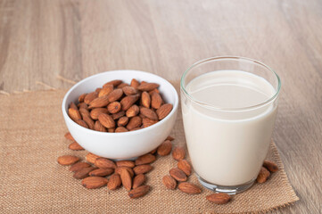 Glass of almond milk with almond in white bowl on table.