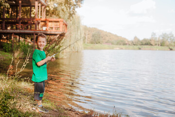 Fototapeta na wymiar A small beautiful boy in a green t-shirt fishing on a fishing rod