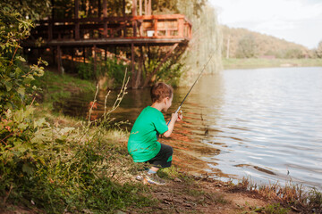 A small beautiful boy in a green t-shirt fishing on a fishing rod