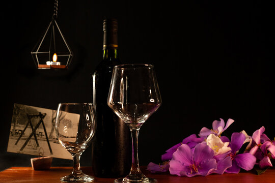 Wooden table with 2 glasses, a bottle of wine, a picture of the park in reverse, hanging candle and purple flowers