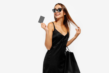 Elegant young business woman in sunglasses, in a black dress, holding shopping bags and a credit card, on a white background, Black Friday, shopping