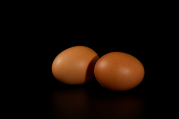 Two brown chicken eggs isolated on black background