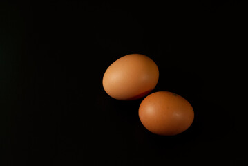 Two brown chicken eggs isolated on black background