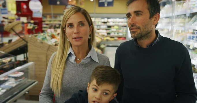 Authentic shot of happy family of father, mother and son are having fun choosing products while shopping for groceries together in supermarket.