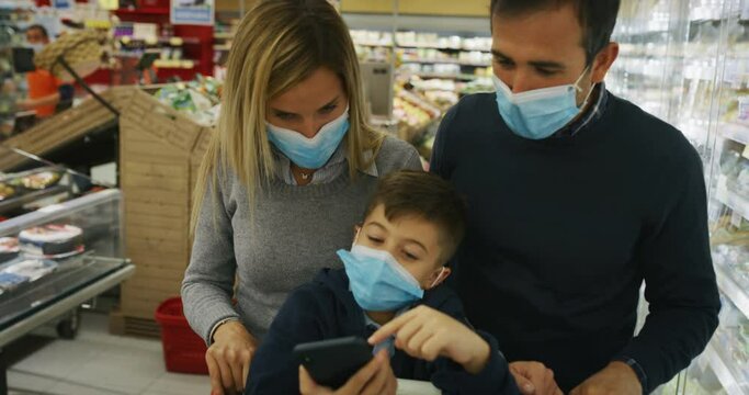 Authentic shot of happy family of father, mother and son wearing medical masks to protect themselves from disease while shopping for groceries together in supermarket.