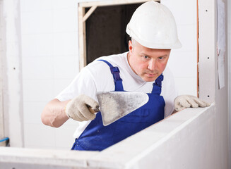 Professional plasterer taping drywall joints with spatula and plaster indoors.