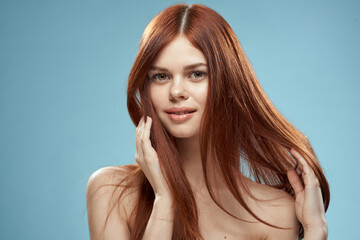 Naklejka premium Pretty woman holding hair in hands grooming naked shoulders cropped view blue background