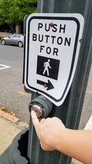 Hand pressing the button at a crosswalk sign.